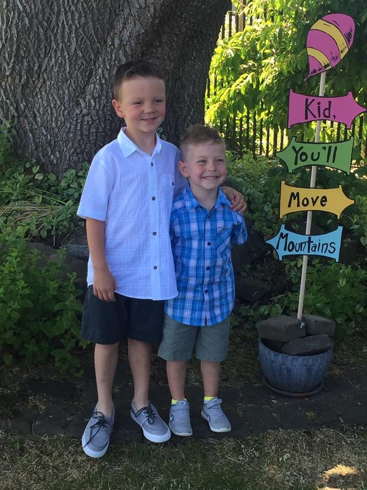 Two brothers by the Kid You'll Move Mountains sign